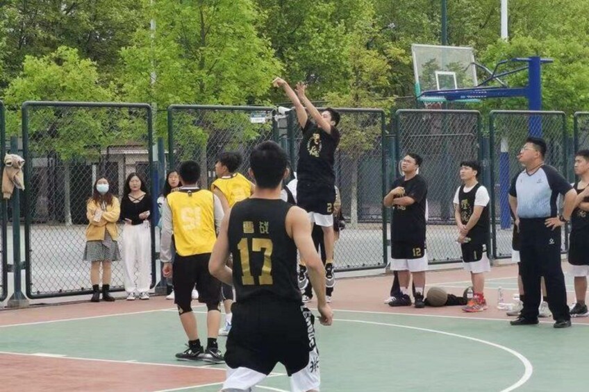 A basketball game with players in black and yellow jerseys on a court, spectators in the background, and a basketball hoop. 4