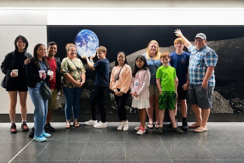 A group of people standing in front of a wall with a large globe. 3