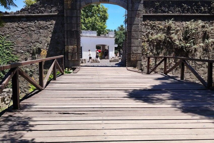A wooden bridge with stone walls on either side, leading to a white building. 3