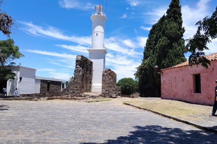 A white lighthouse, a stone wall, and a pink building. 4