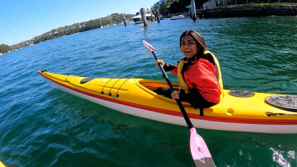 Une personne pratiquant le kayak sur une étendue d’eau, avec une ville côtière en arrière-plan. 1