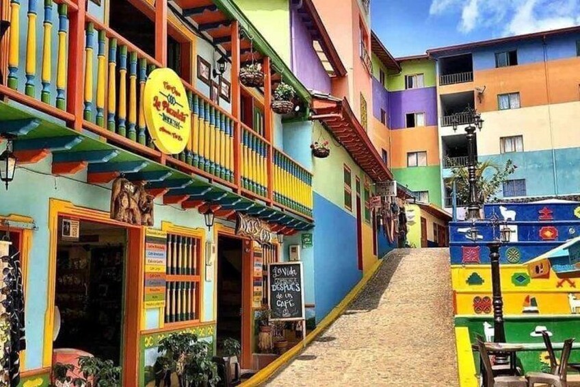 A colorful street with buildings painted in various bright colors, a sign for a restaurant, and a staircase leading up to a building. 1