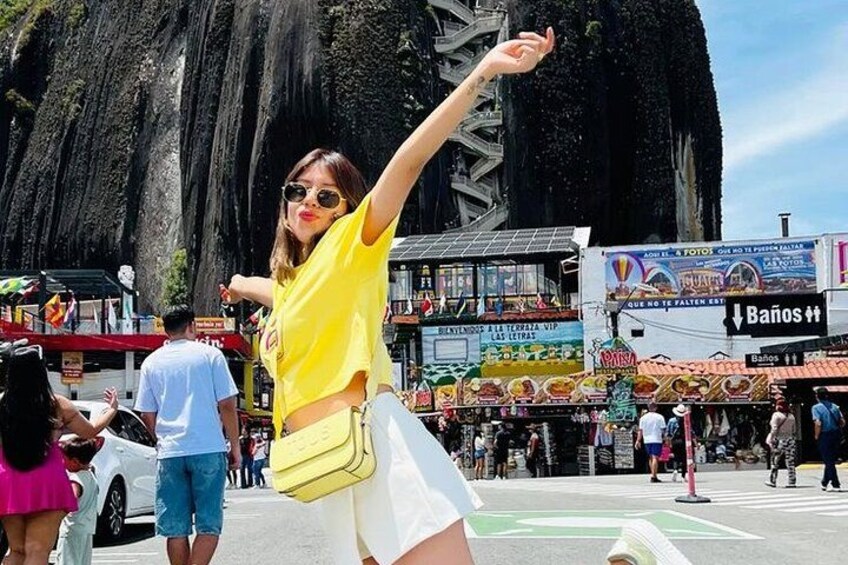 A person in a yellow top and white shorts, a yellow bag, and a large rock formation in the background. 2