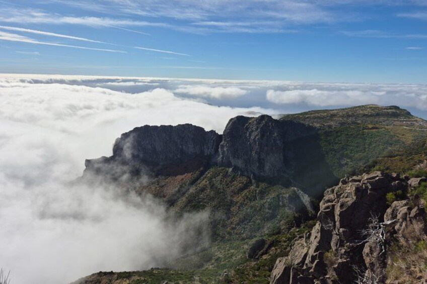 A mountainous landscape with rocky cliffs and a layer of clouds below. 1