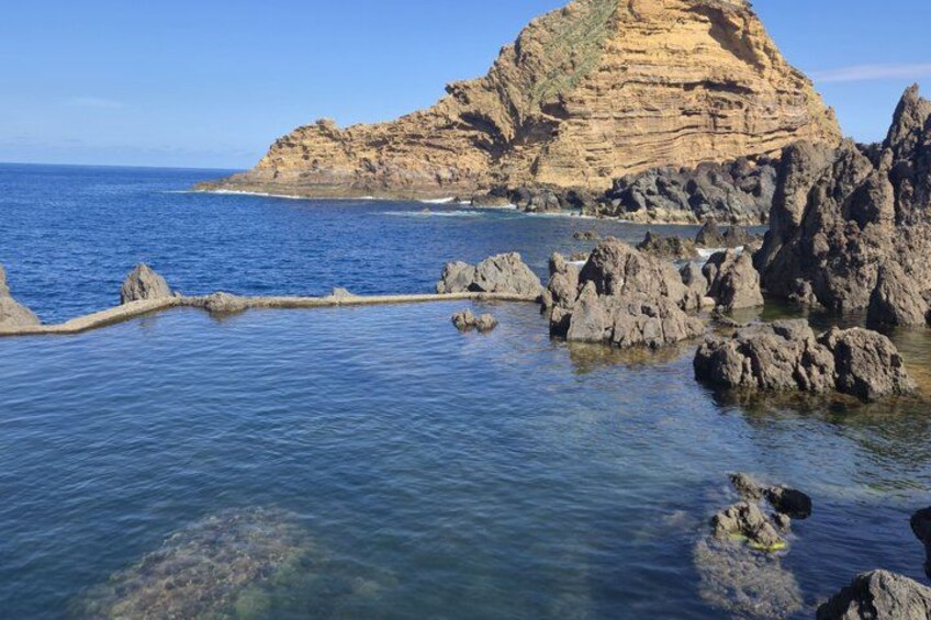 A coastal landscape with a prominent cliff, clear blue sea, and rocky outcrops. 4