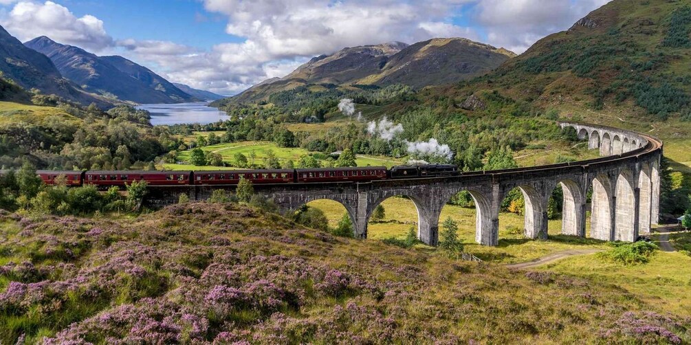 Un train circule sur un viaduc en pierre dans une région montagneuse, avec un lac en arrière-plan. 1