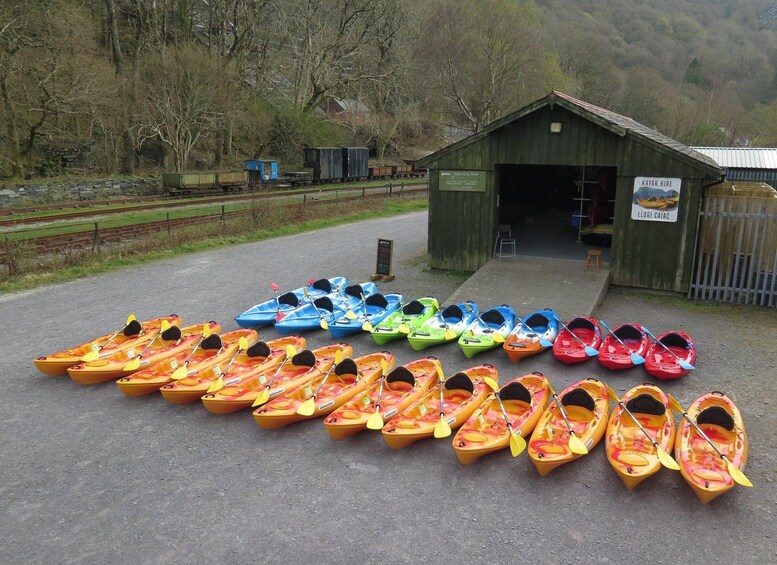 A row of colorful kayaks lined up on a gravel path with a wooden building in the background. 2