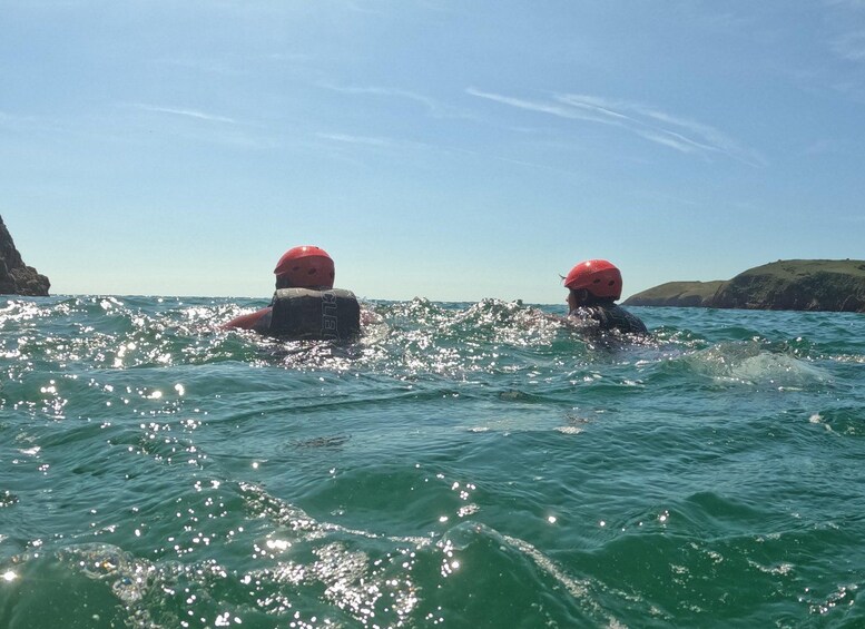 Two people swimming in the ocean with a rocky coastline in the background. 2