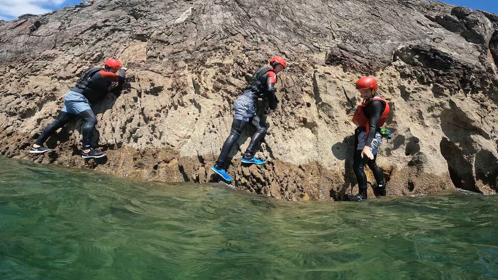 Three people jumping off a rocky cliff into a body of water. 1
