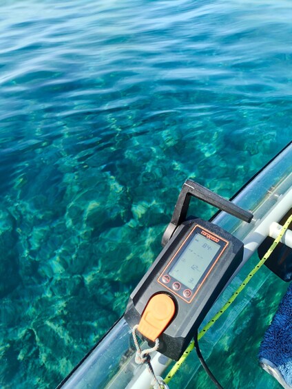 A water testing device on a boat with clear water and submerged rocks. 2