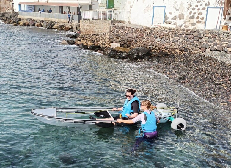 Two people in a kayak on a river, with a rocky shore and buildings in the background. 3