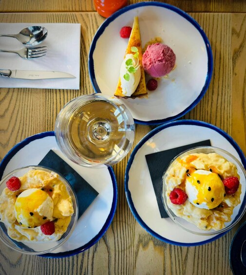 Three dessert plates with ice cream and fruit, a glass of wine, and cutlery on a wooden table. 2