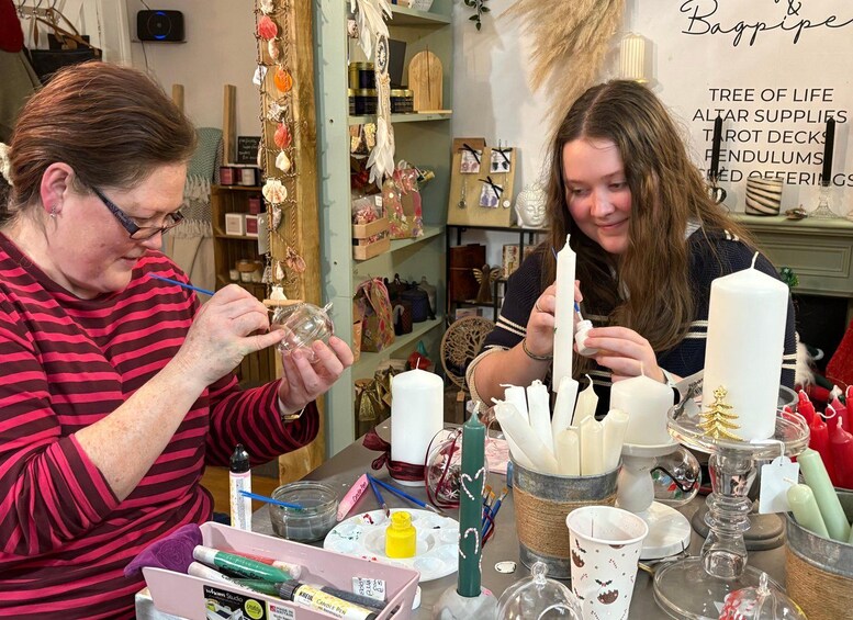 Two people crafting candles in a workshop with various supplies and decorations. 3