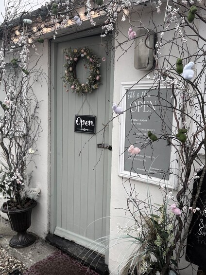 A quaint shop with a grey door, a 'Open' sign, and a window displaying various items. 1