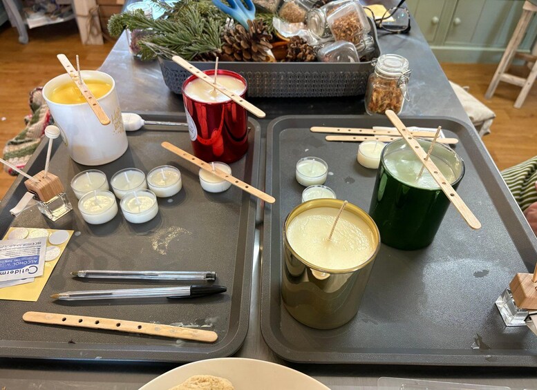 A table with various candles, a large green candle, and a red candle. There are also small jars and a box of pine cones. 5