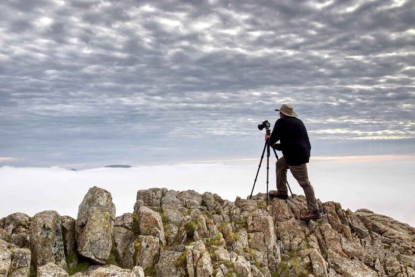 A person with a camera on a tripod standing on rocky terrain with a cloudy sky above. 5