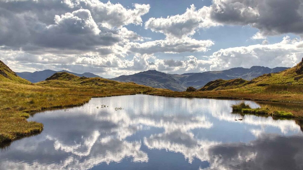 A tranquil lake surrounded by grassy hills and mountains under a partly cloudy sky. 1