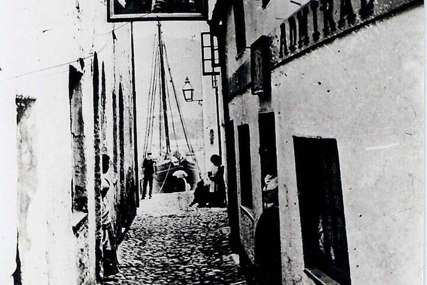 A narrow cobblestone street with buildings on either side, a hanging sign, and a lantern. 3