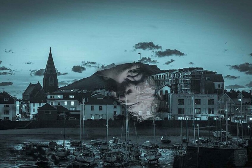 A coastal town with a prominent church spire, a large building with signage, and boats in the water. 1