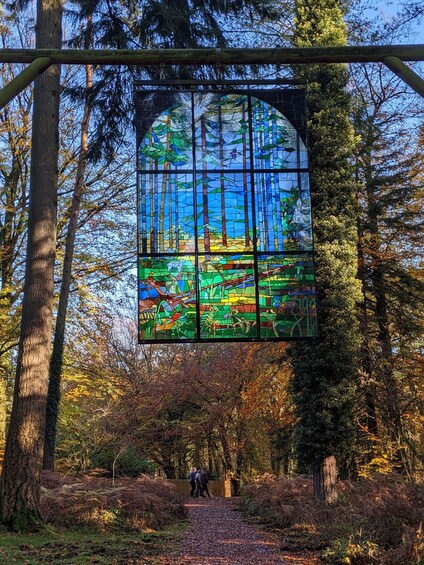 A stained glass window depicting a forest scene, with a pathway leading to it surrounded by trees. 5
