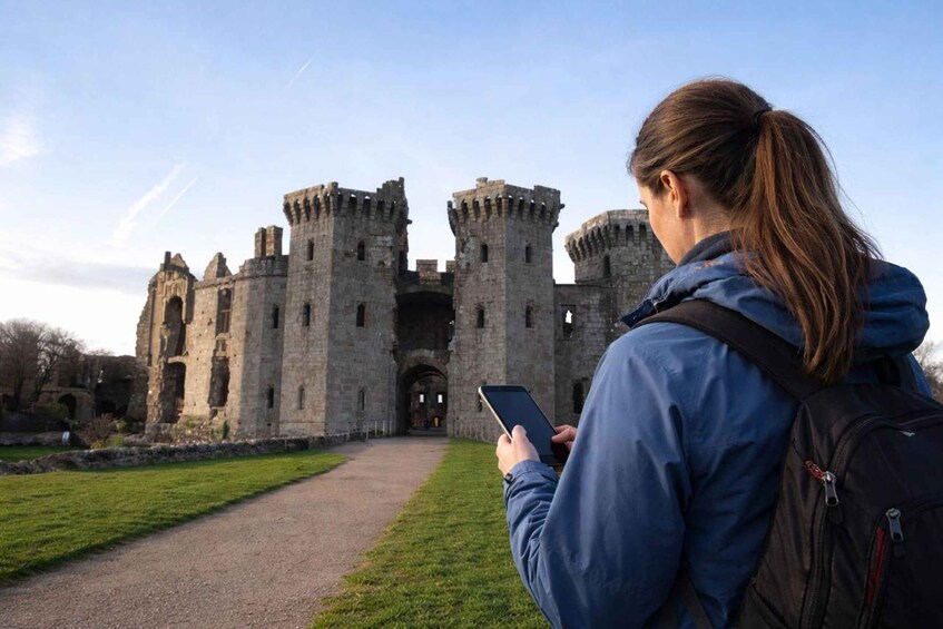 A woman using a smartphone in front of a historic castle with a paved path leading to the entrance. 1