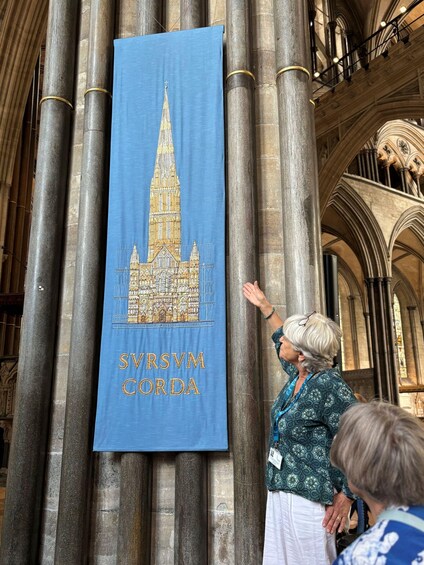 A person standing in front of a blue banner with a cathedral illustration and the text 'SVRSVM CORDA' on a historic building with large columns. 2