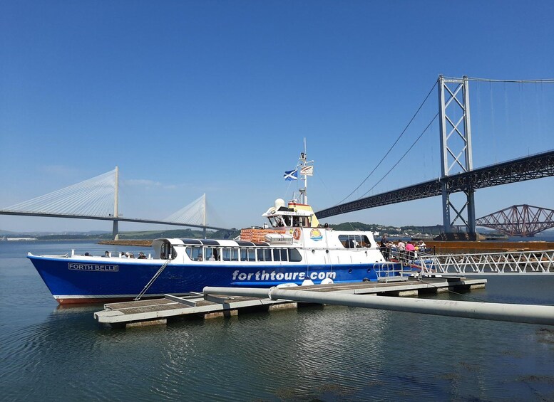 A blue boat named 'Forth Belle' docked at a pier with a bridge in the background. 3