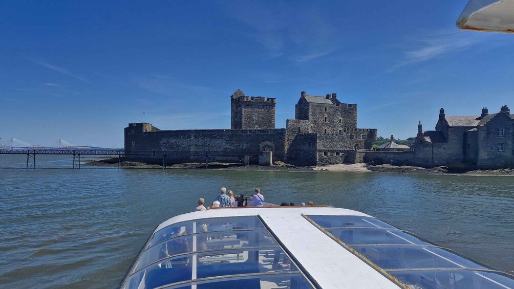 A boat with people on board, a stone castle, and a bridge in the background. 1