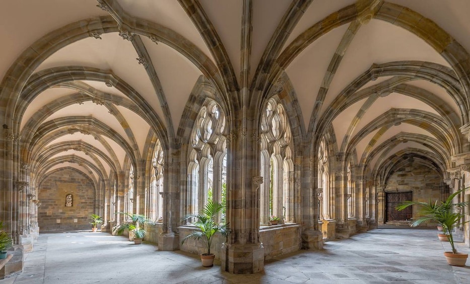 A cloister with stone arches and columns, potted plants, and a stone wall with a statue. 1