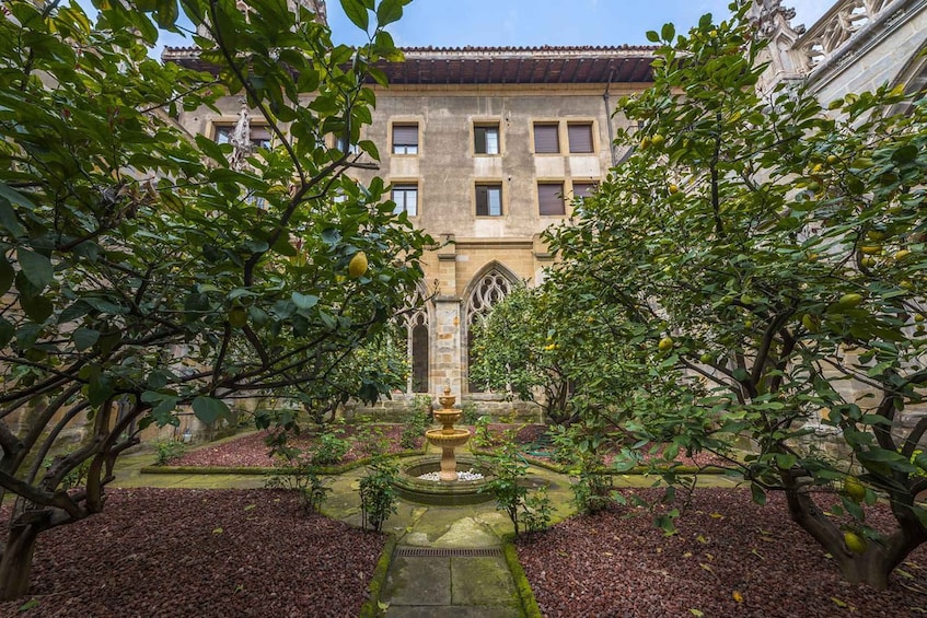 A courtyard with a fountain, surrounded by trees and a building with a tiled roof. 2