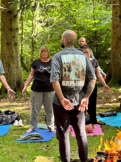 A group of people practicing yoga outdoors on mats with a forest background and a campfire. 3