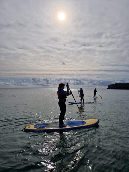 Una persona haciendo paddleboard en aguas tranquilas, con un cielo nublado y un acantilado distante. 4