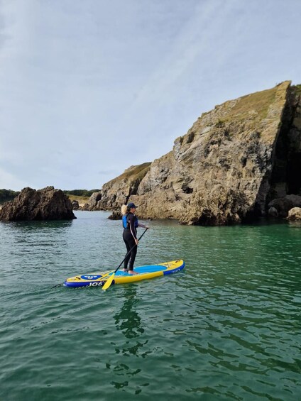 Una persona haciendo paddleboard en un cuerpo de agua, con acantilados rocosos al fondo. 3