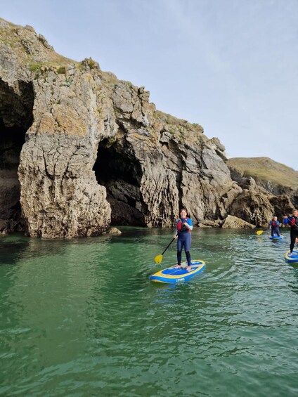 Personas haciendo paddleboard cerca de una costa rocosa con una formación parecida a una cueva. 1