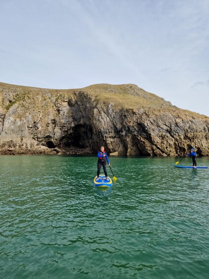 Dos personas haciendo paddleboard en aguas tranquilas, con acantilados rocosos al fondo. 5