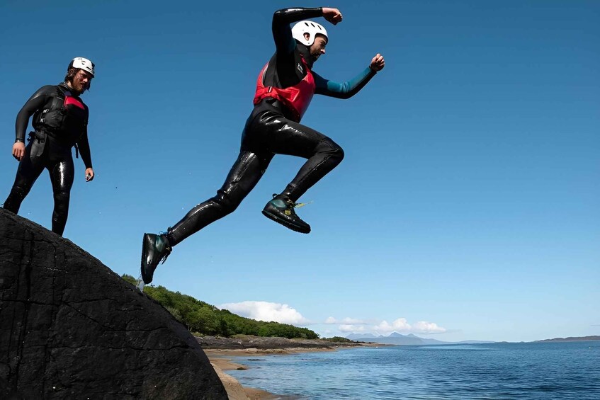 Two people in wetsuits jumping off a cliff into the water. 1
