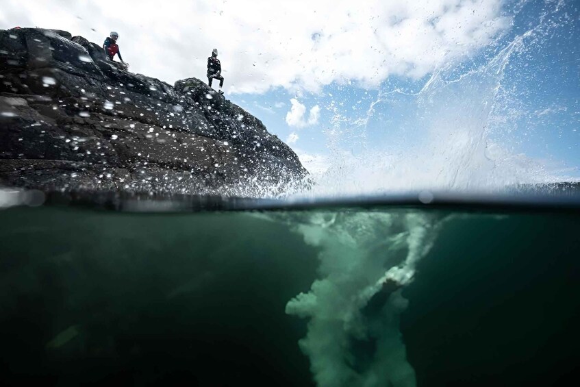 A person standing on a rocky cliff with a wave crashing below. 5