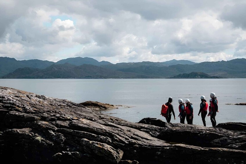 A group of people hiking on rocky terrain near a lake with mountains in the background. 2