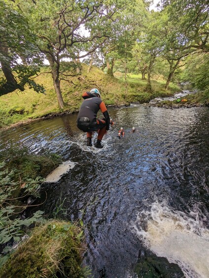 A person wading through a shallow stream in a forested area. 5