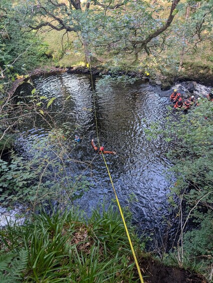 A group of people rappelling down a water body surrounded by greenery. 2