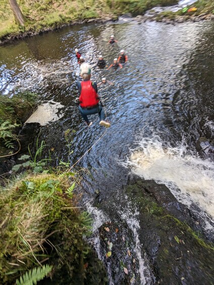 A person in a red life jacket wading through a river with others in the background. 4
