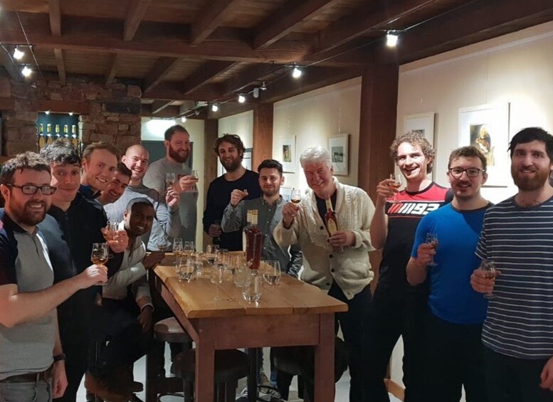 A group of people gathered around a wooden table with glasses, in a room with exposed wooden beams and stone walls. 4