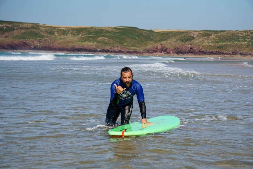 A person in a blue wetsuit standing in shallow water with a green surfboard. 3