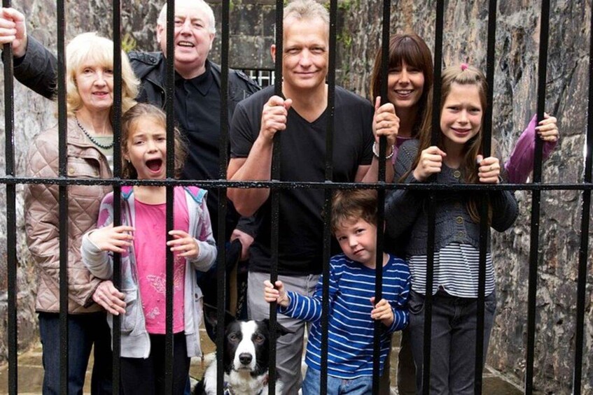A group of people standing behind a metal fence with a dog in the foreground. 2