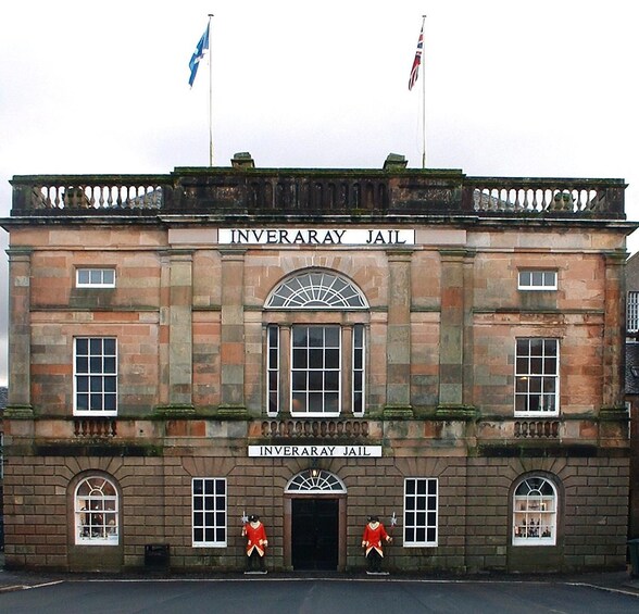 The Inveraray Jail building with two flags, a sign, and two statues. 4