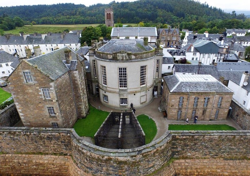 A historic town with a prominent round tower, surrounded by traditional stone buildings and a well-maintained green space. 5