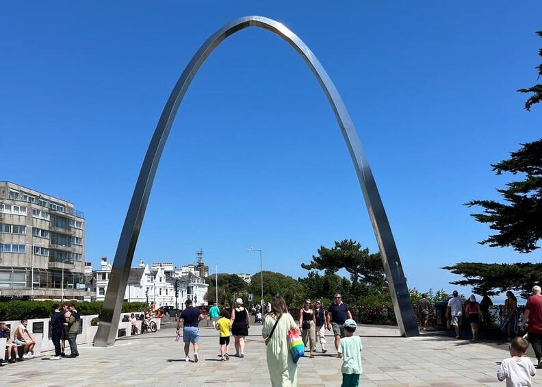Une grande structure arquée en métal se dresse sur une place publique, et des gens se promènent autour. 5