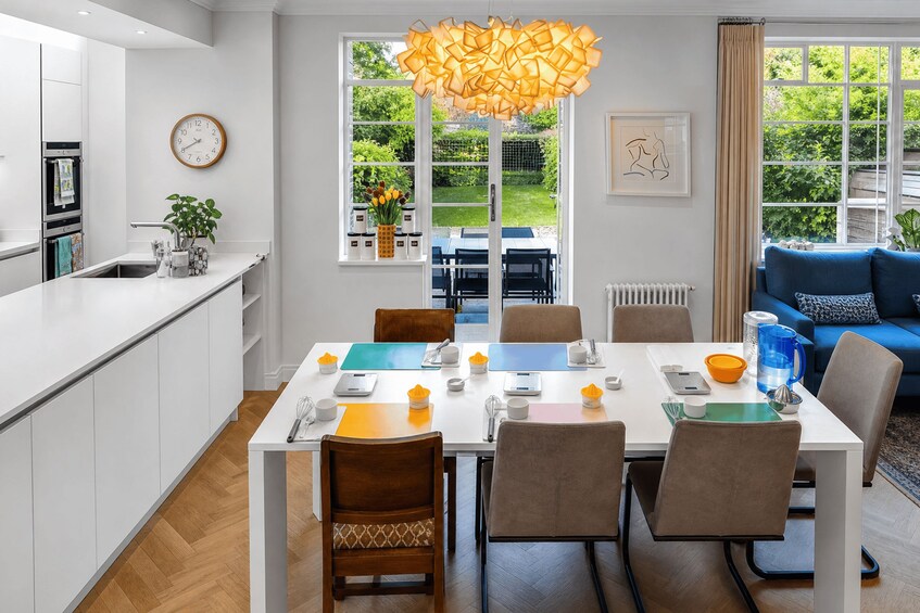 A modern kitchen with white cabinets, a dining table set for six, and a large window with a view of the garden. 5