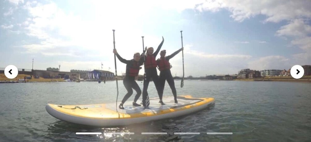 Three people on a paddleboard in a body of water, with buildings in the background. 3