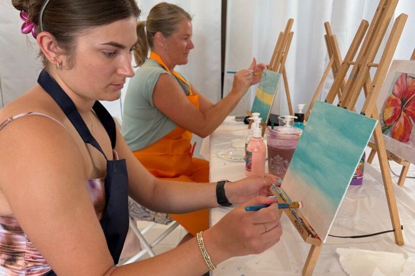 Two people painting on easels with art supplies on a table. 5